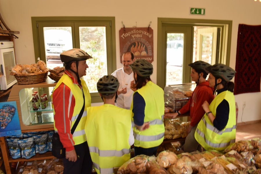 tourist cyclists inside Aristaios' store with bread products, cookies, talking with employee and tasting delicacies